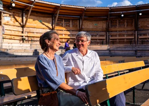 Couple souriant assis sur des bancs en bois, avec la Berlin WelcomeCard et le bus hop-on hop-off