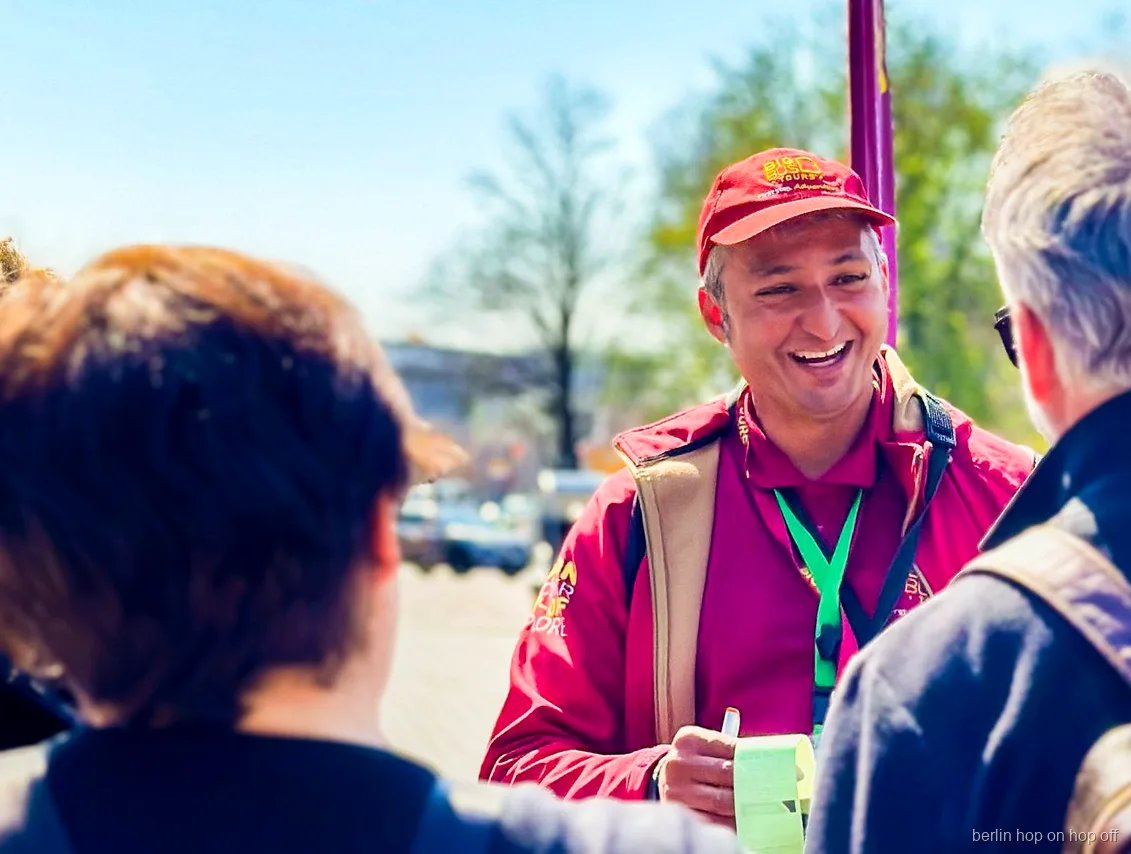 Smiling Big Bus Berlin hop on hop off staff member in a red cap talking with visitors outdoors
