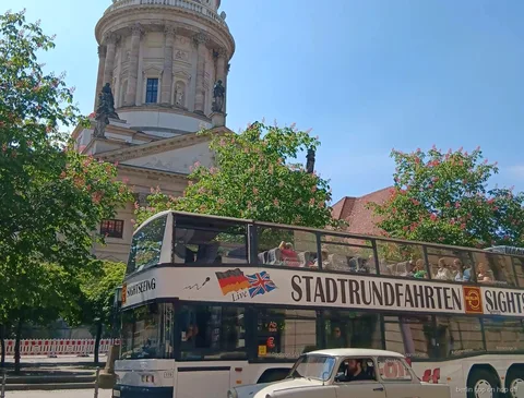 Bus Sightseeing hop on hop off de Berlín i un cotxe clàssic crema davant una església amb cúpula i arbres florits