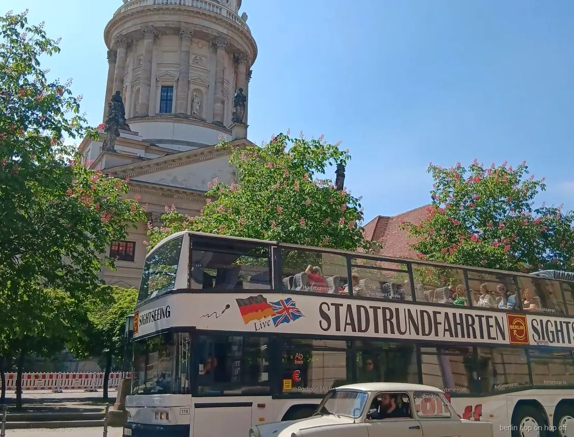 Bus Sightseeing hop on hop off de Berlín i un cotxe clàssic crema davant una església amb cúpula i arbres florits