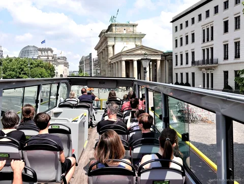 Pasajeros en la cubierta abierta del bus hop on hop off de Berlín mirando hacia la Puerta de Brandeburgo