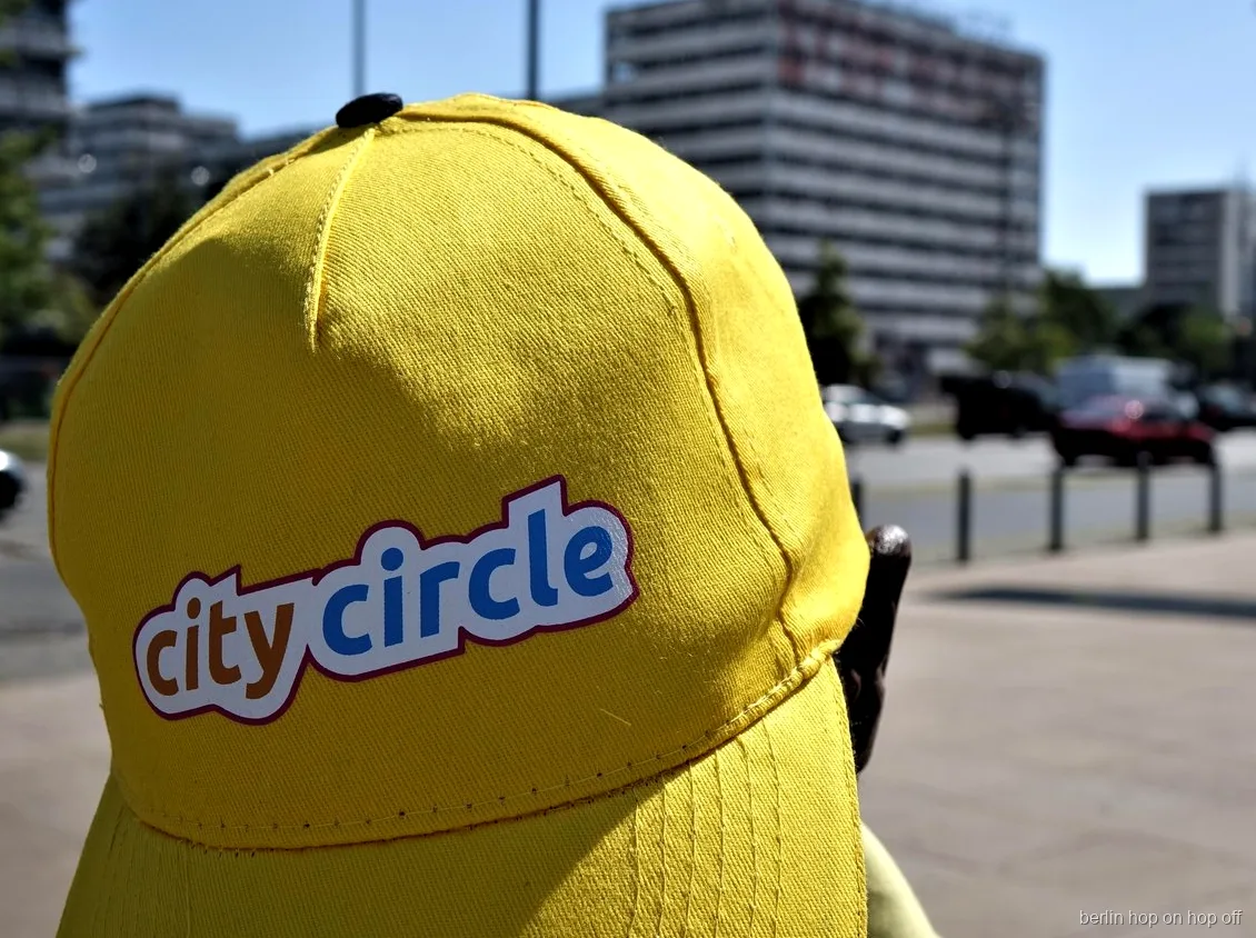 Primer plano de una gorra amarilla City Circle con logotipo en una calle soleada, bus hop on hop off de Berlín