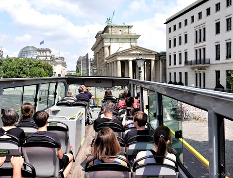 Passengers on the open top deck of a Berlin hop on hop off bus looking toward the Brandenburg Gate