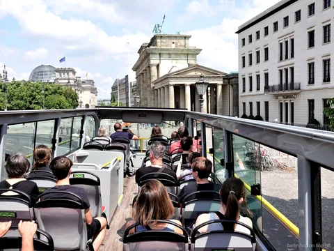 Passagiers op het open dak van de Berlijn hop on hop off bus kijken naar de Brandenburger Tor
