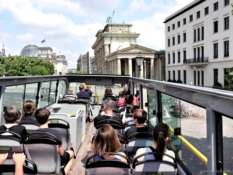 Pasażerowie na otwartym pokładzie autobusu hop on hop off w Berlinie patrzą na Bramę Brandenburską