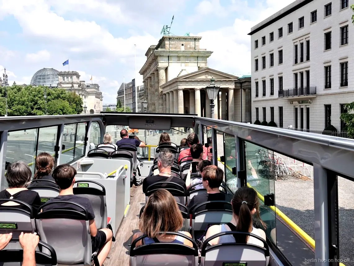 Pasażerowie na otwartym pokładzie autobusu hop on hop off w Berlinie patrzą na Bramę Brandenburską