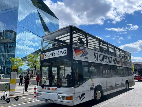Biały piętrowy autobus Stadtrundfahrten Sightseeing hop on hop off w Berlinie obok szklanego budynku