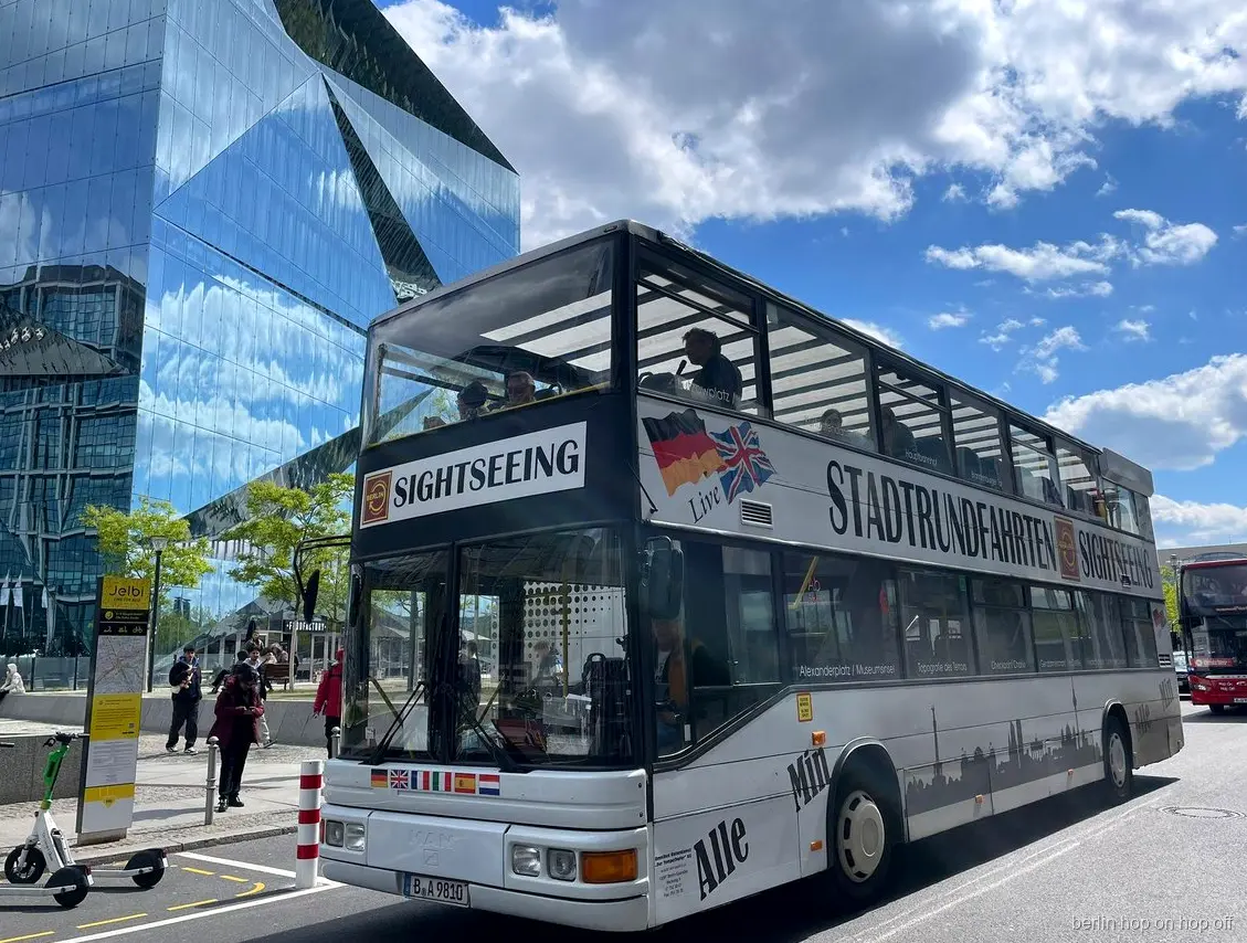 Biały piętrowy autobus Stadtrundfahrten Sightseeing hop on hop off w Berlinie obok szklanego budynku
