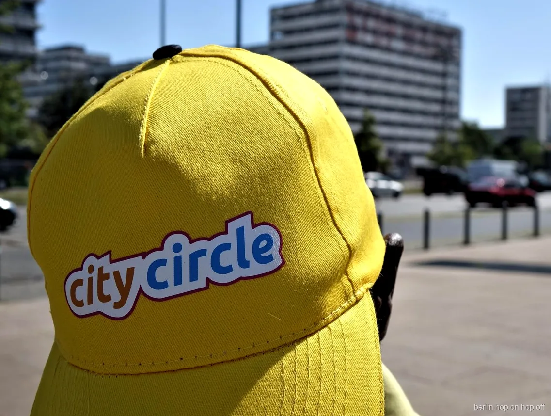 Primo piano di un cappellino giallo City Circle con logo in una strada soleggiata, bus hop on hop off di Berlino