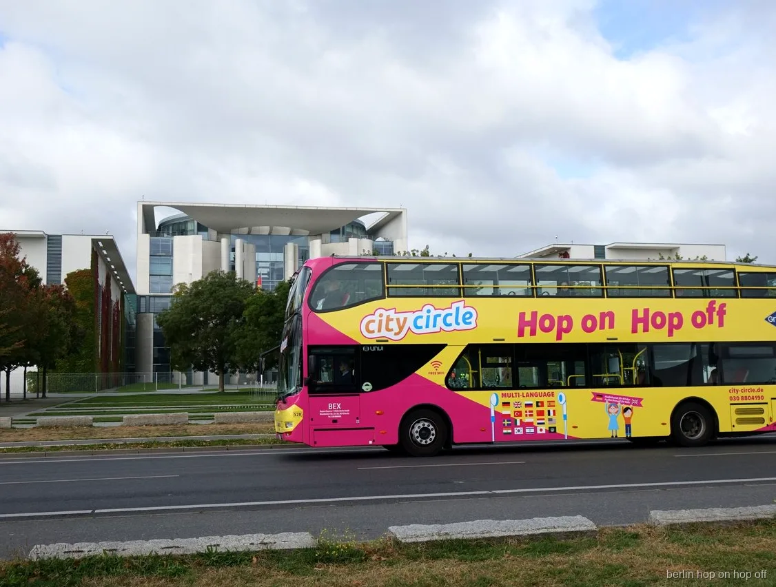 Roze en gele City Circle Berlijn hop on hop off dubbeldekker rijdt langs de Bondskanselarij