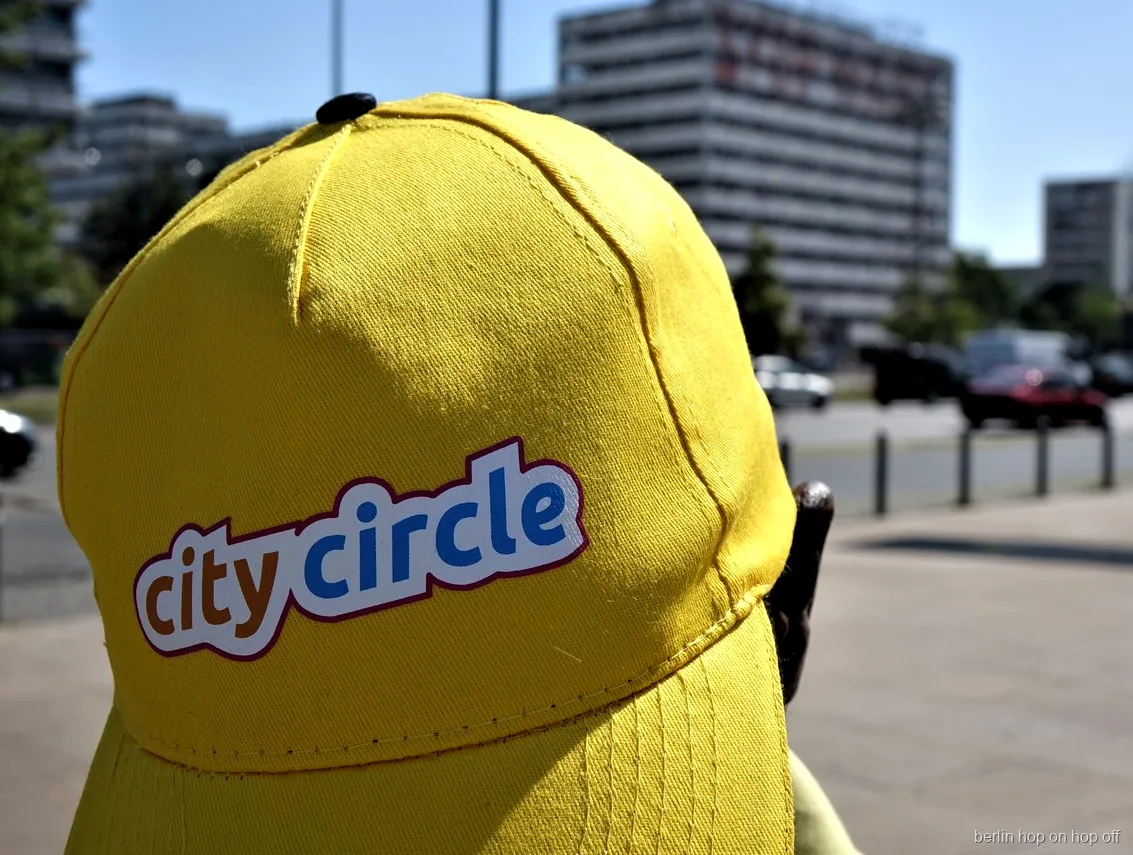 Primo piano di un cappellino giallo City Circle con logo in una strada soleggiata, bus hop on hop off di Berlino