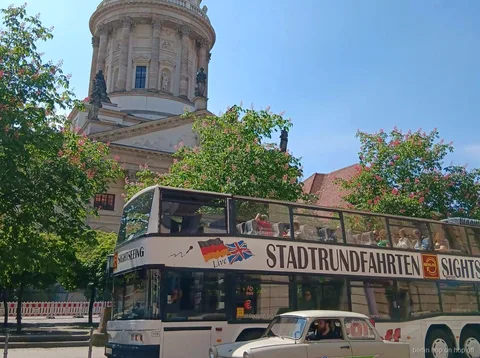 Berlin hop on hop off Sightseeing bus og en cremefarvet veteranbil ved en kirke med kuppel og blomstrende træer