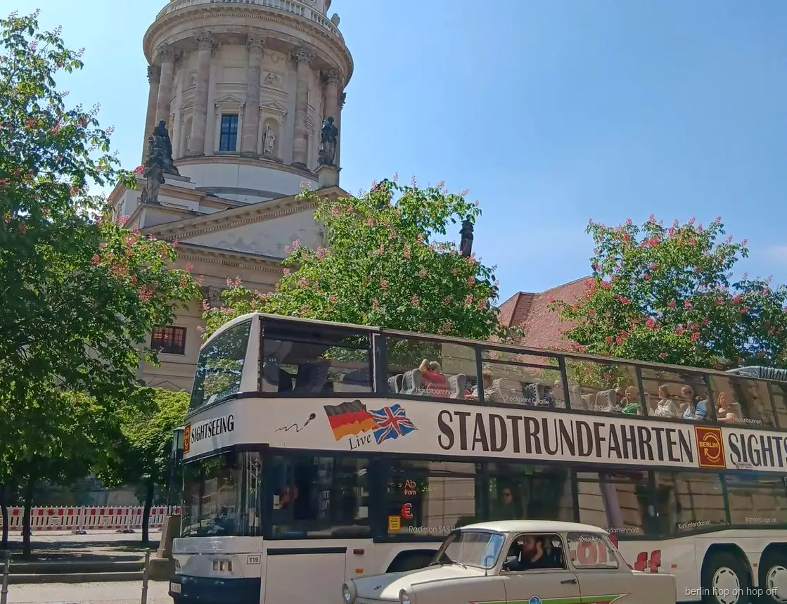Berlin hop on hop off Sightseeing otobüsü ve krem rengi klasik araba, kubbeli kilise ve çiçekli ağaçlar yanında