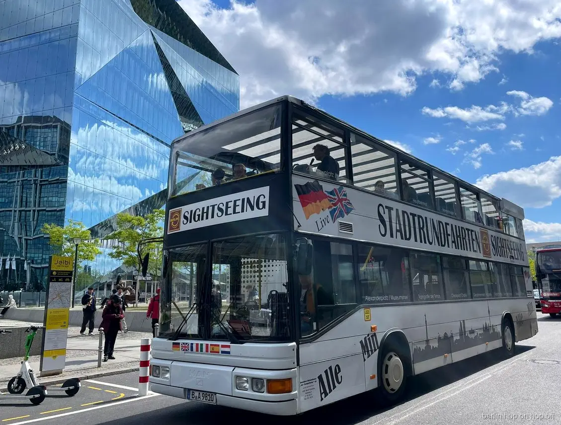 Weißer Stadtrundfahrten Sightseeing Doppeldeckerbus der Berlin Hop on Hop off Tour vor einem Glasgebäude