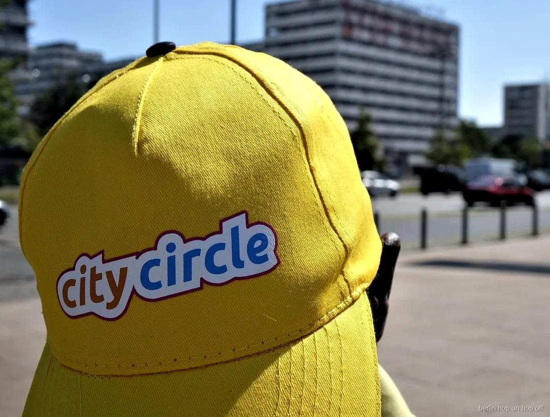 Nahaufnahme einer gelben City Circle Kappe mit Logo auf sonniger Straße, Berlin Hop on Hop off Bus